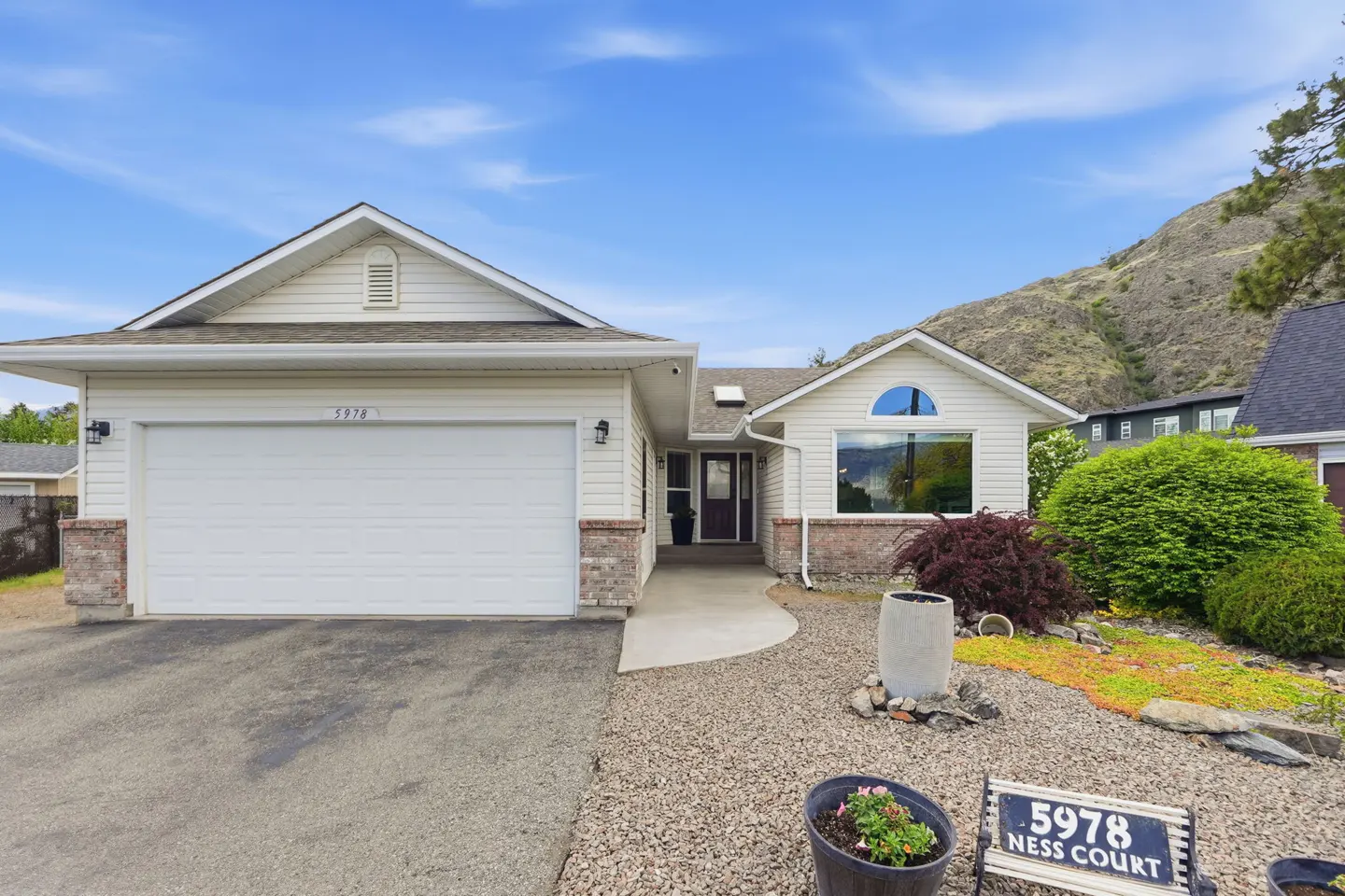 Exterior view of a one-story home with white siding, a two-car garage, and a well-maintained front yard with a sign reading "5978 Ness Court."