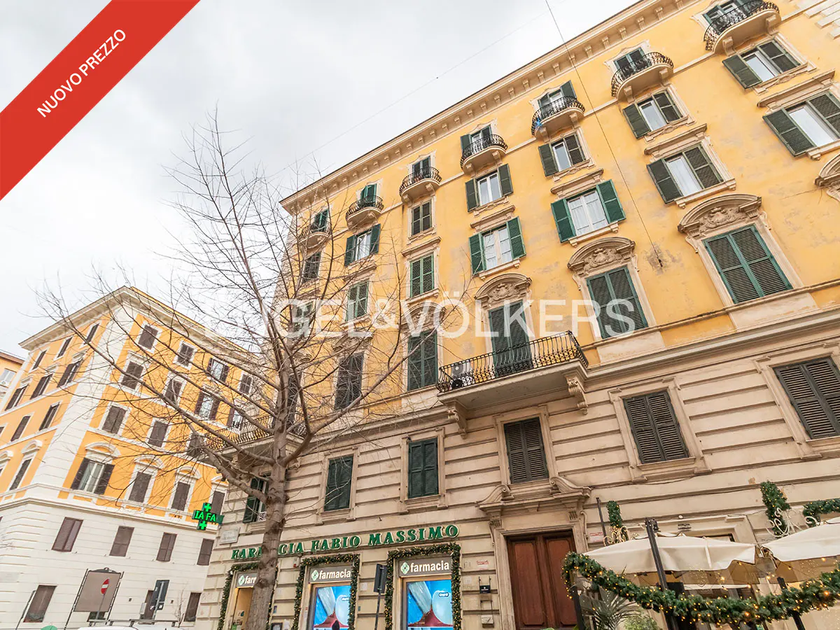 Exterior view of a yellow building with green shutters and balconies, with a pharmacy on the ground floor.