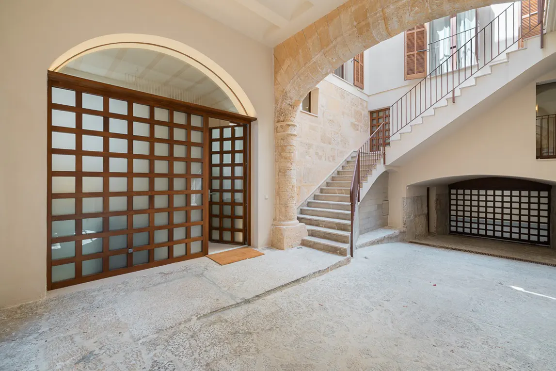 Interior courtyard with stone archway, stairs, and wood-framed glass doors. The floor is concrete.
