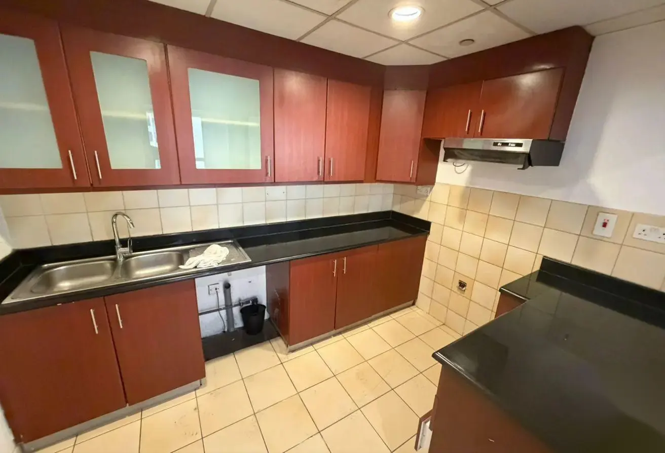A kitchen with brown cabinets, black countertops, a stainless steel sink, and beige tiled floors.