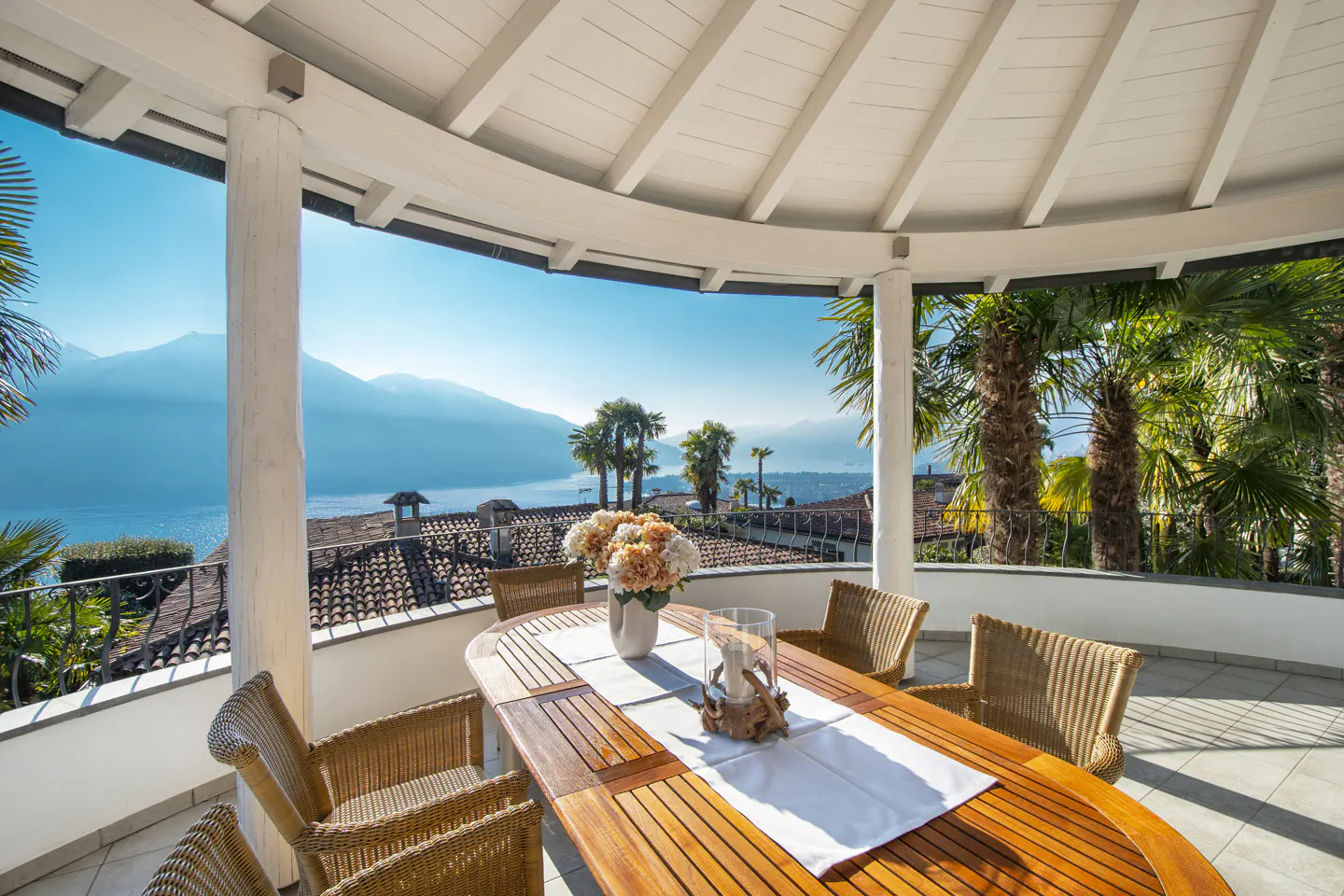 Outdoor patio with a wooden table, wicker chairs, and a view of a lake and mountains.