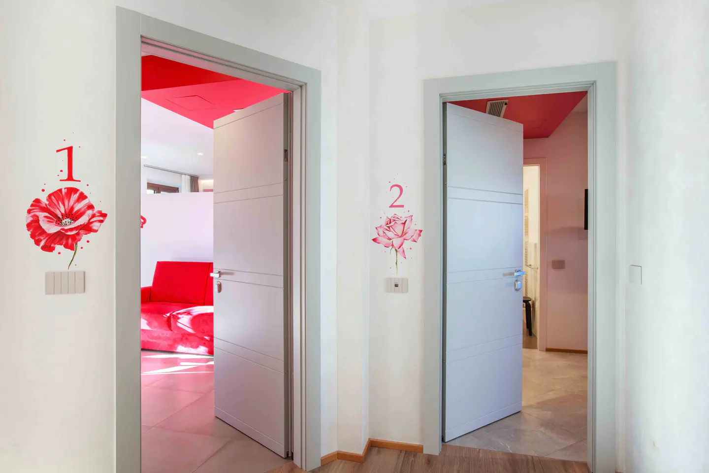 Hallway with two white doors, labeled with floral decals numbered 1 and 2, leading into rooms with bright red ceilings.