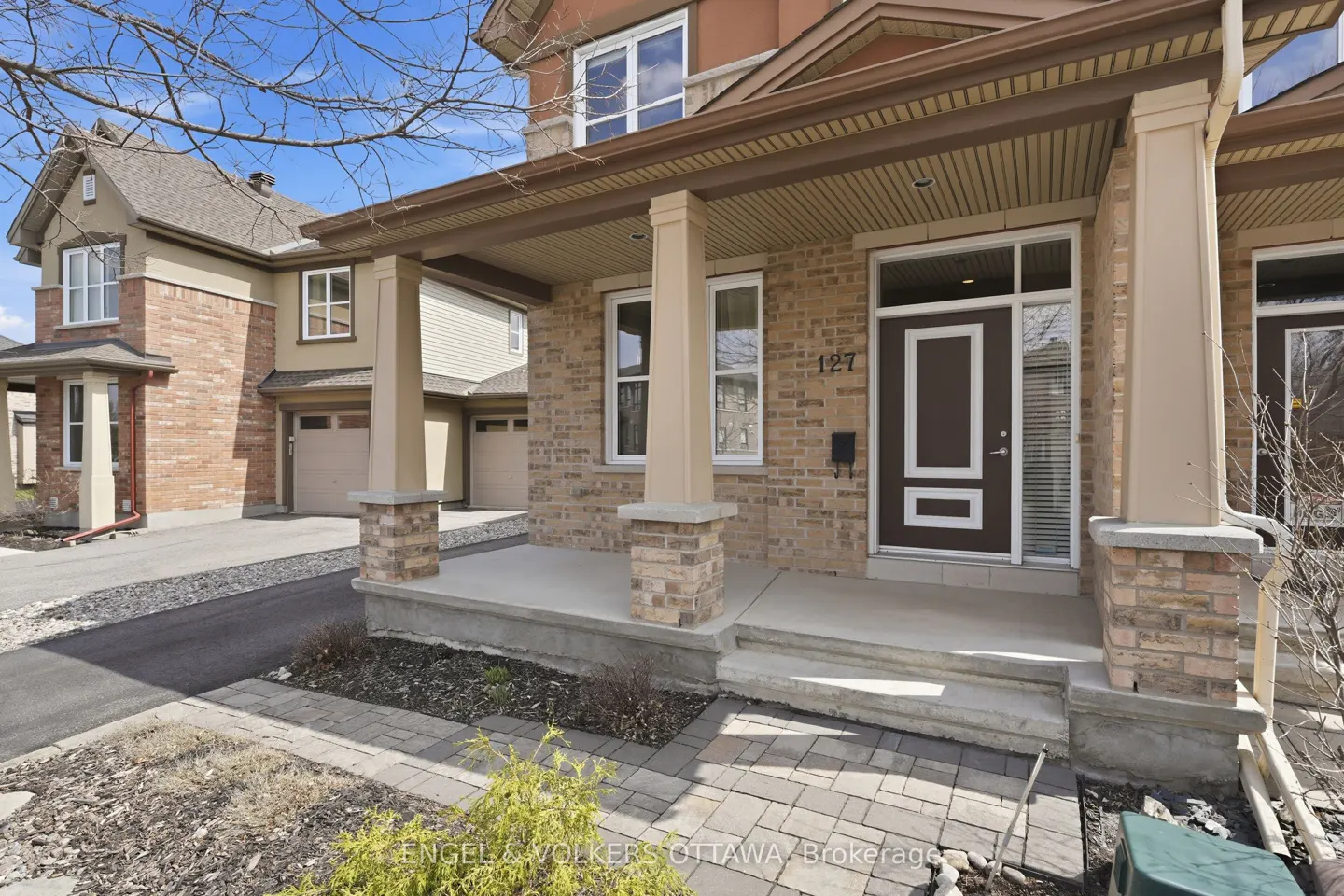 Exterior view of a two-story brick townhouse with a covered porch and brown door with the number 127 above it.