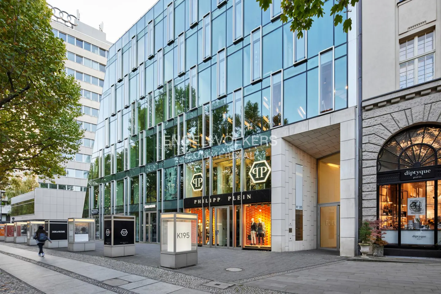 Modern glass-fronted commercial building with a Philipp Plein storefront on a city sidewalk with display cases.