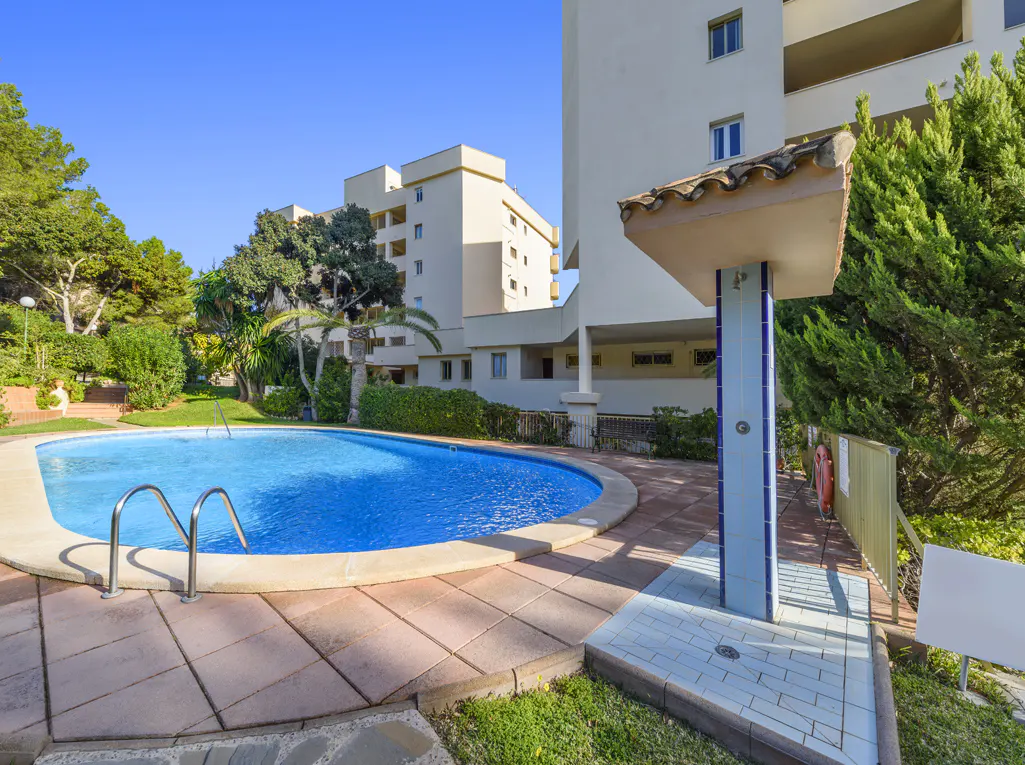 Outdoor swimming pool with blue water, metal ladder, and a poolside shower, set against a modern apartment building.