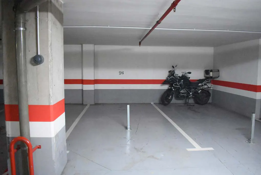 A parking space in a garage with a black motorcycle parked in the back. The walls are painted gray and white with a red stripe.