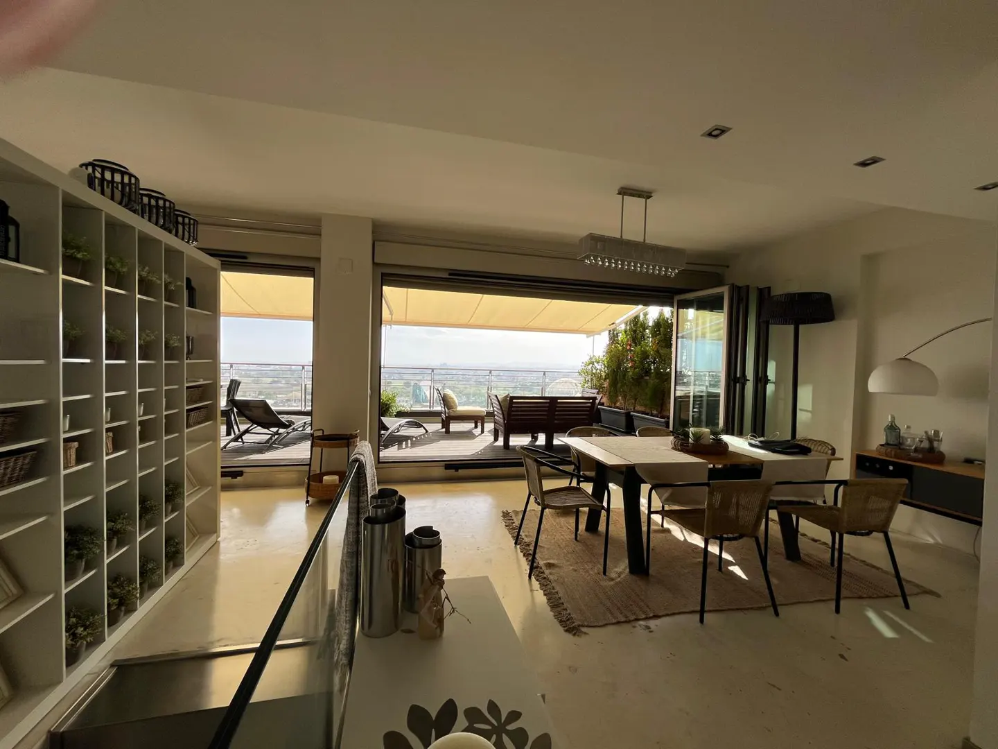 Modern dining area with a table and chairs, opening to a balcony with outdoor furniture and a scenic landscape view.