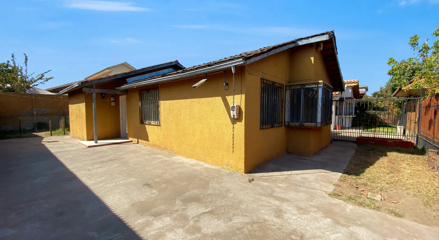 A yellow, one-story house with barred windows and a concrete driveway under a blue sky.