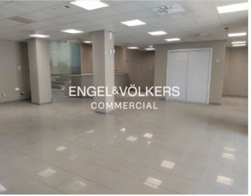 Empty commercial space with gray tile floor, gray walls, white columns, and white doors. Engel & Volkers logo is superimposed.