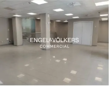 Empty commercial space with gray tile floor, gray walls, white columns, and white doors. Engel & Volkers logo is superimposed.