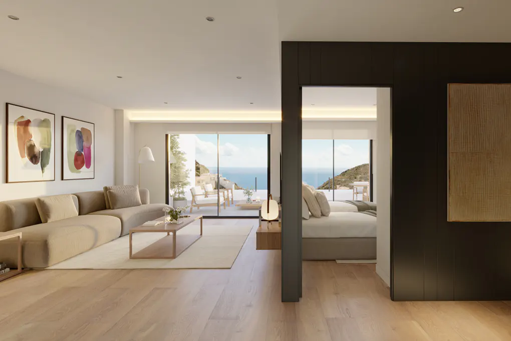 Open-concept living space with a beige sofa, wood floors, and ocean view. A bedroom is visible through a doorway.