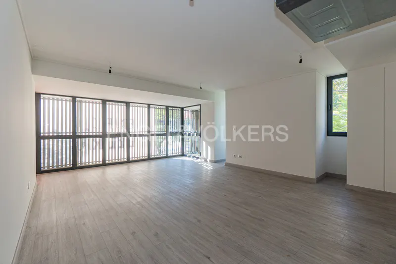Bright, empty room with gray wood floors, white walls, and a large window wall with black frames. A smaller window is on the right.