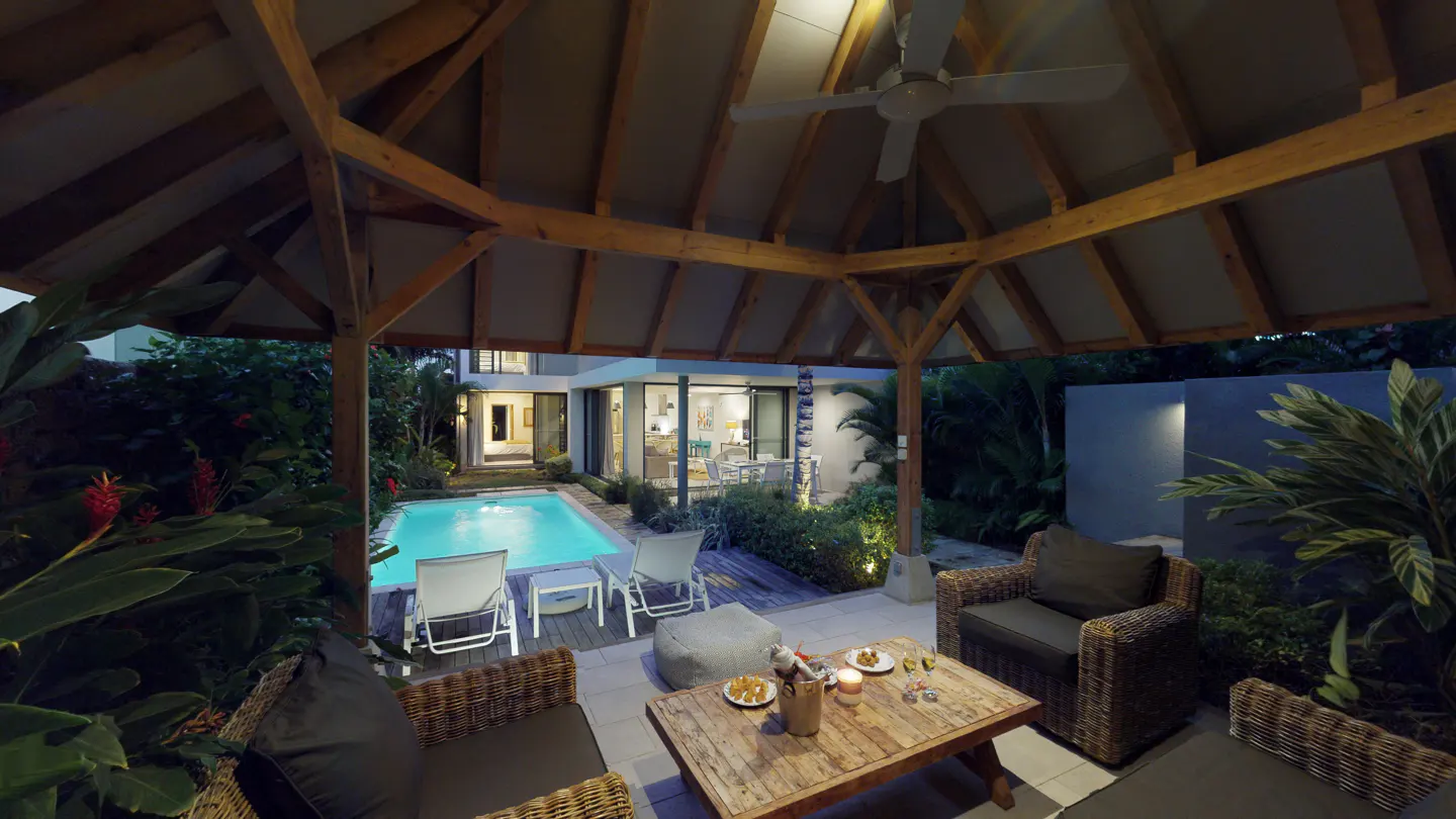 Outdoor patio with a wooden gazebo, wicker furniture, and a pool in the background. A ceiling fan is visible in the gazebo.