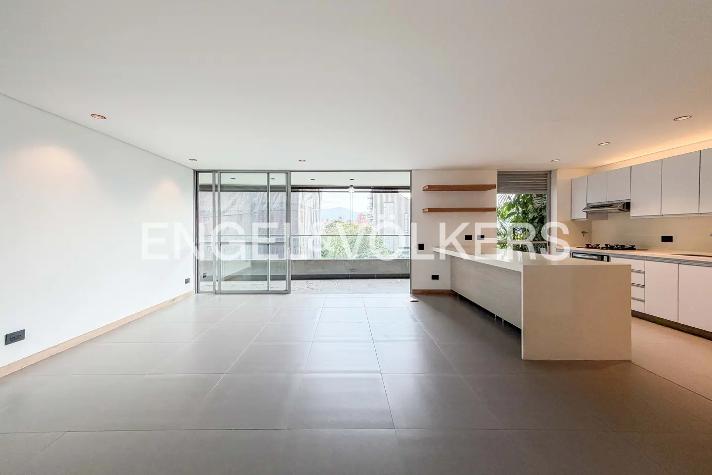 Bright, modern apartment with gray tile floors, white walls, and a kitchen with white cabinets and island. Sliding glass doors lead to a balcony.