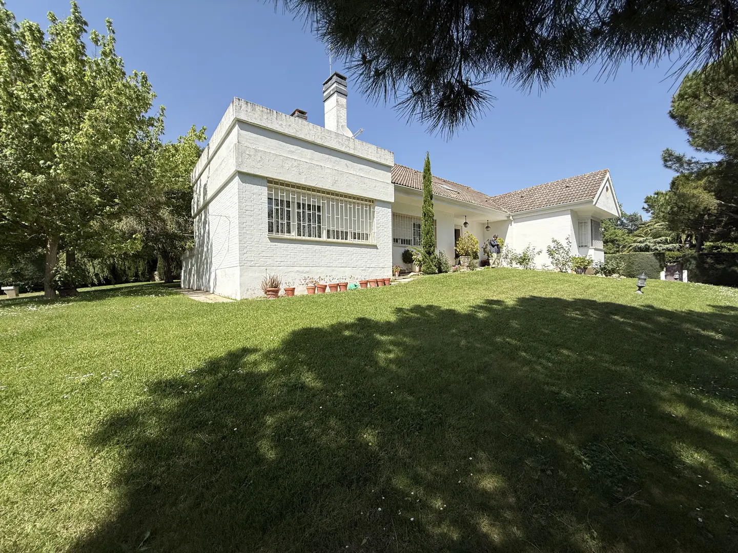 Exterior view of a white house with a chimney, surrounded by a green lawn and trees under a blue sky.