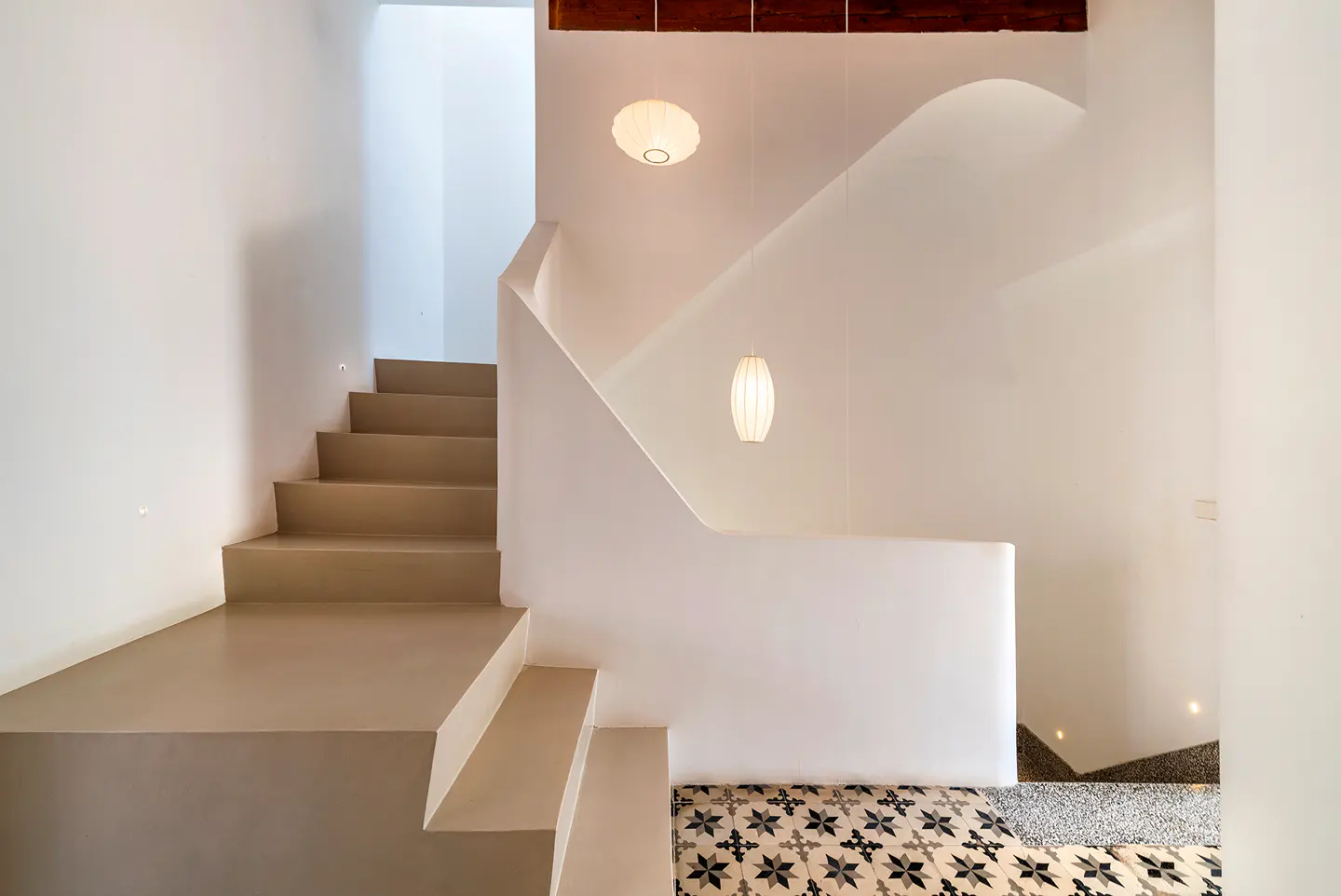 Modern staircase with beige steps, white walls, and two hanging pendant lights above a patterned tile floor.