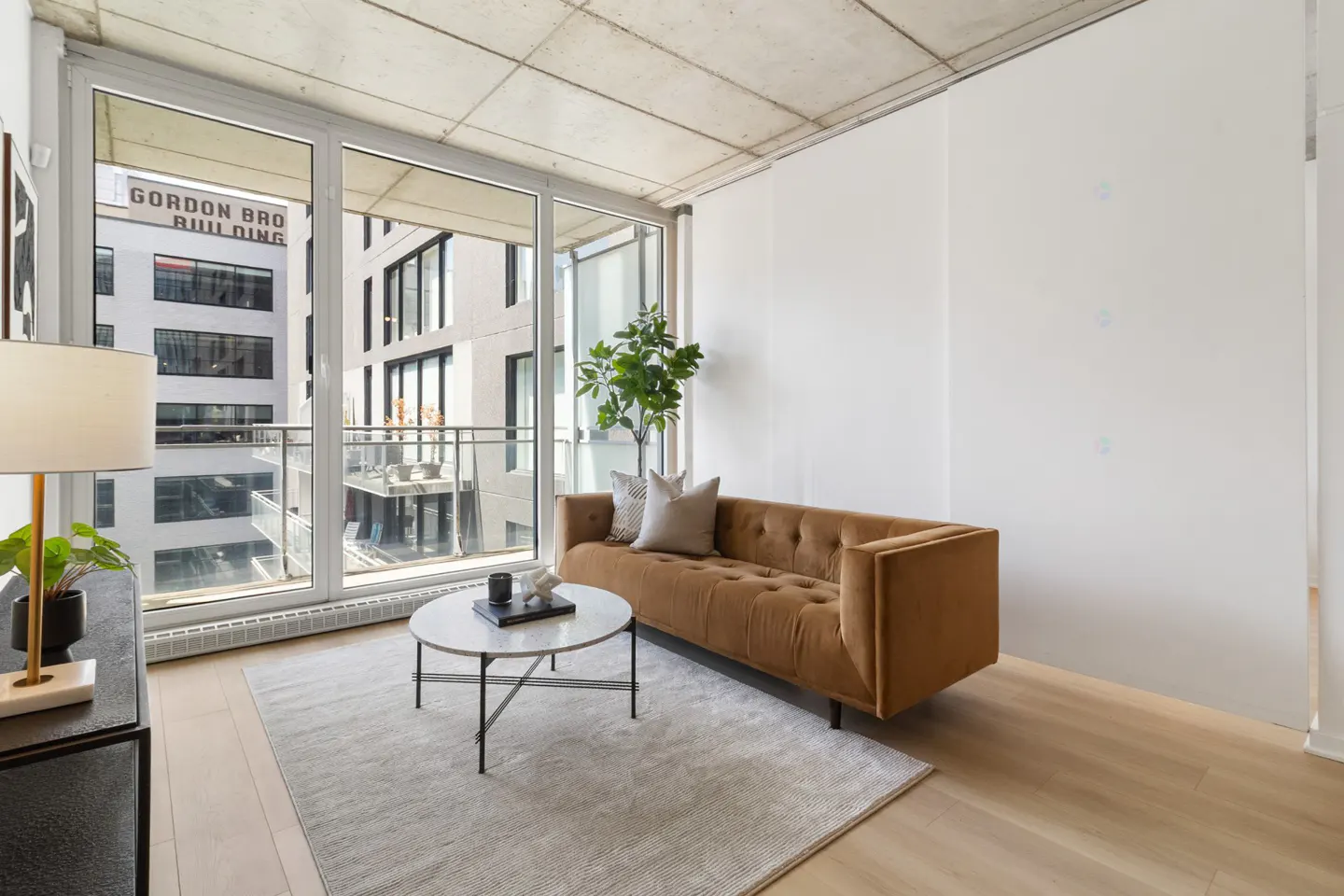 Living room with a brown sofa, marble coffee table, and large windows overlooking a city building.
