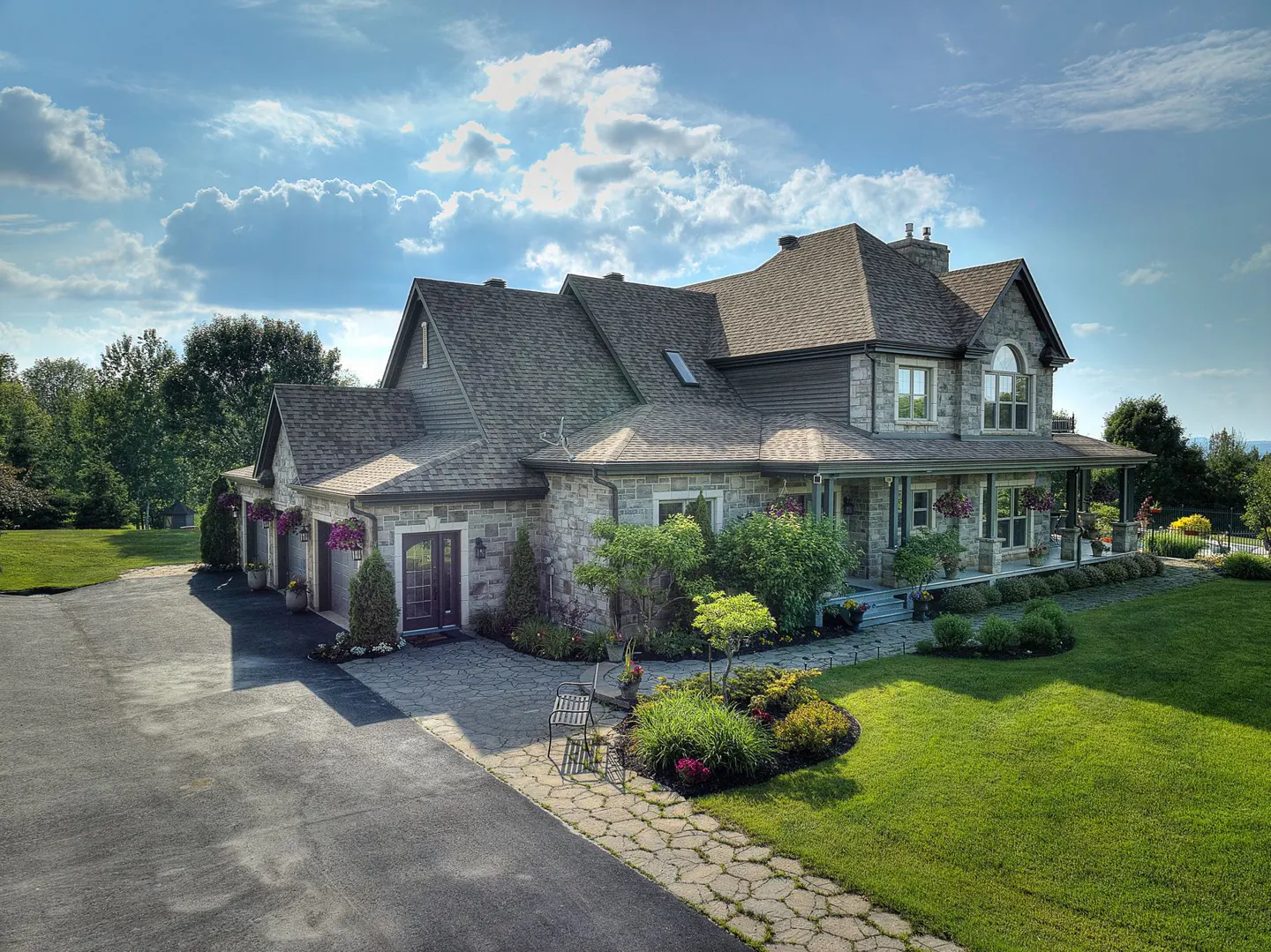 Stone house with a long porch, green lawn, and blue sky with clouds.