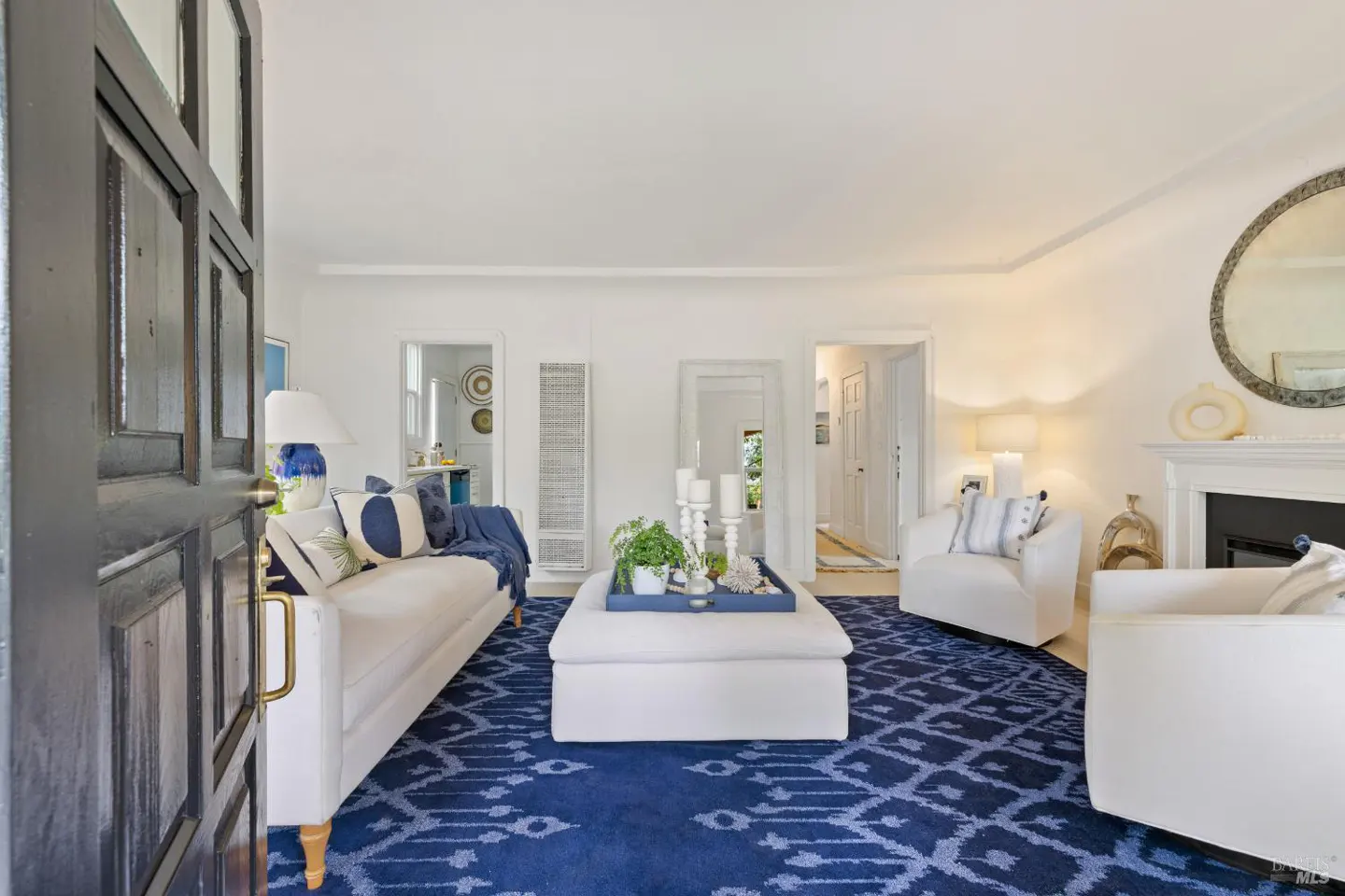 Open black door reveals a bright living room with white furniture, blue patterned rug, and a fireplace.
