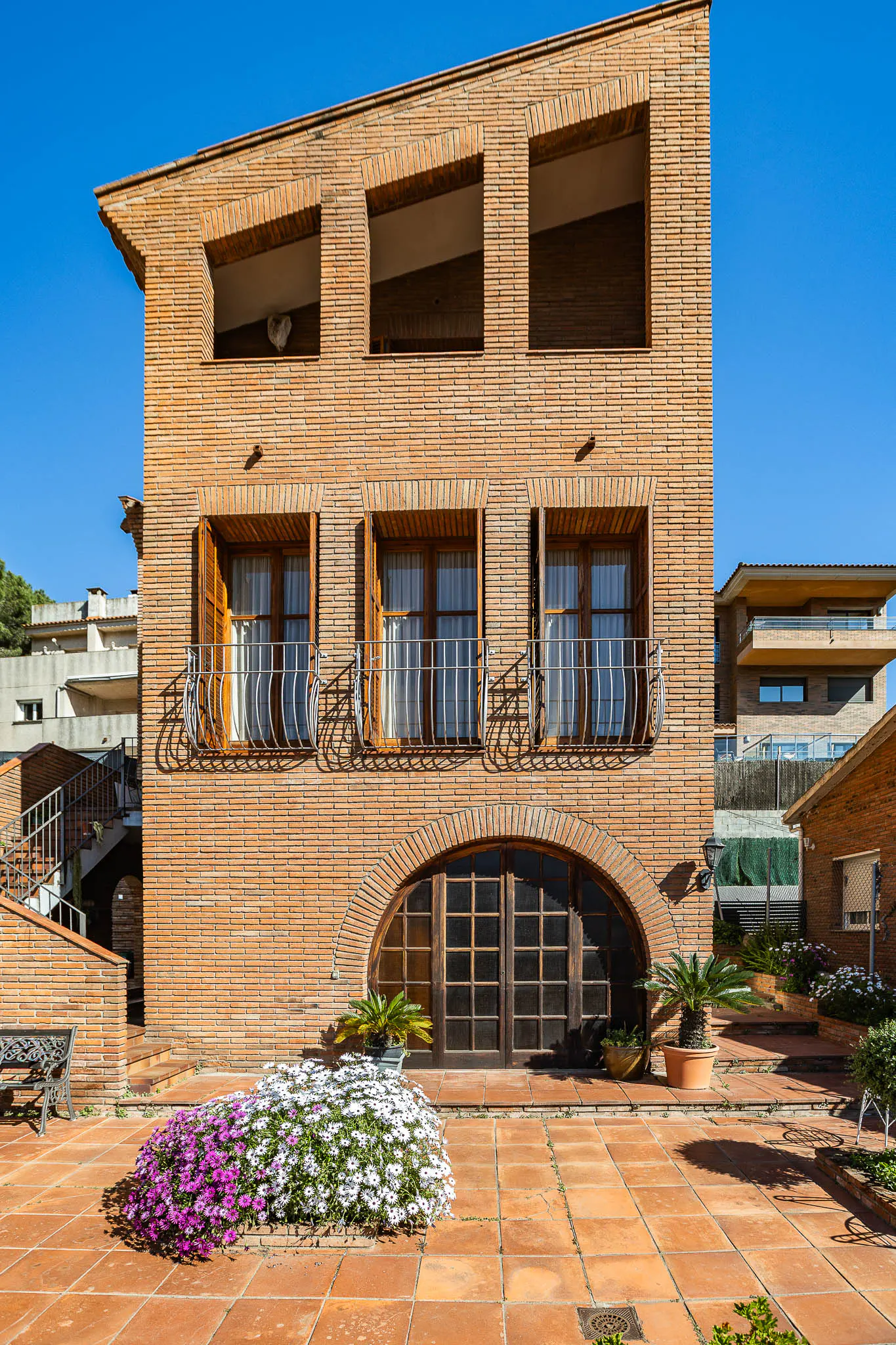 Exterior of a three-story brick house with an arched window and a tiled patio with flowers.