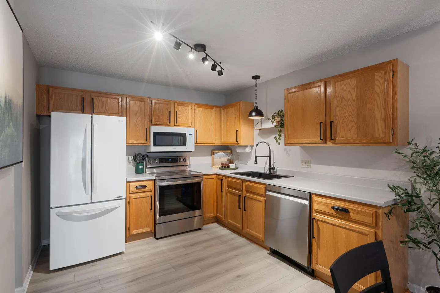 Bright kitchen with wood cabinets, stainless steel appliances, and light gray walls. Track lighting and a pendant lamp illuminate the space.