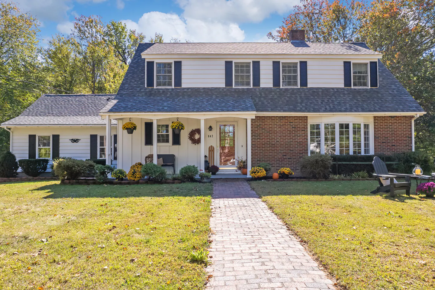 Two-story house with brick and white siding, dark shutters, and a brick walkway leading to the front door.