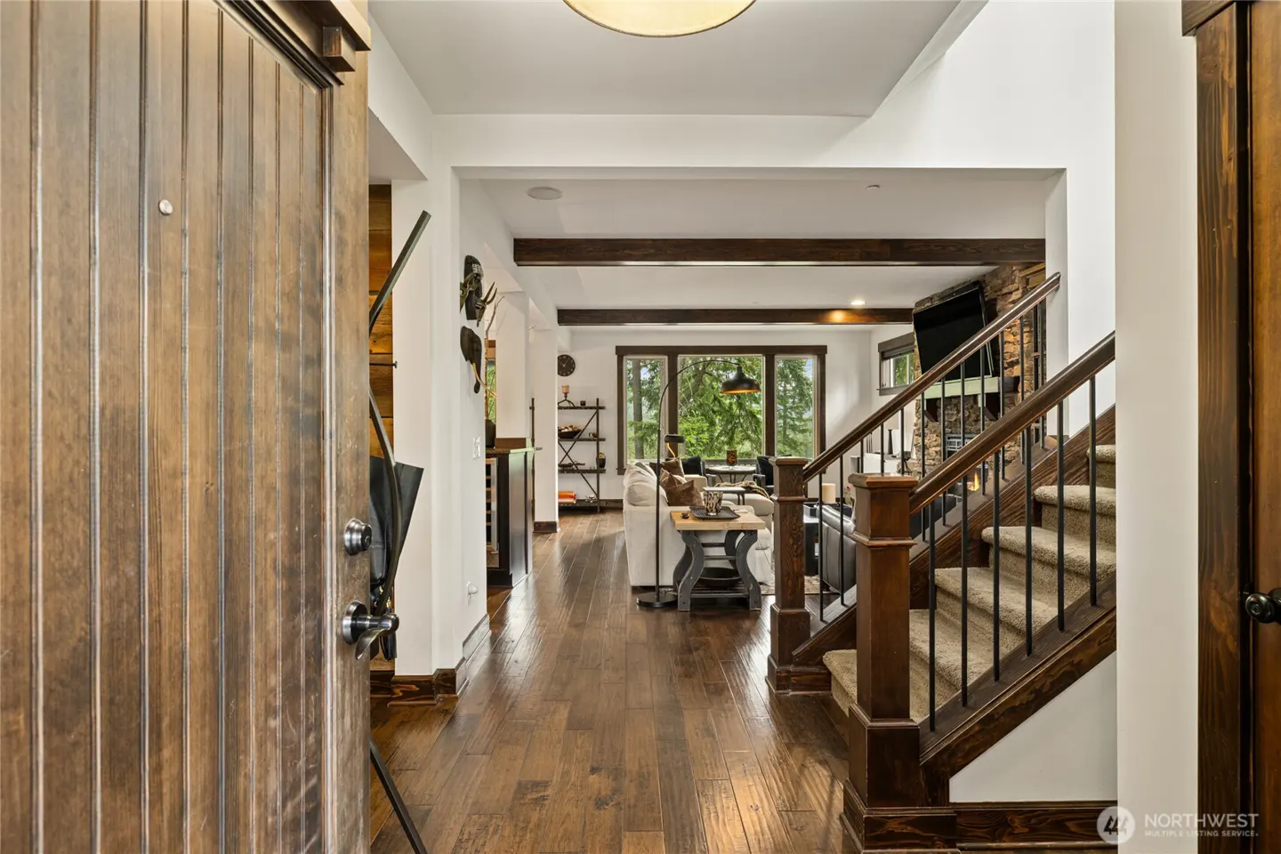 View from a wooden front door into a home with hardwood floors, a carpeted staircase, and a living room with a fireplace.