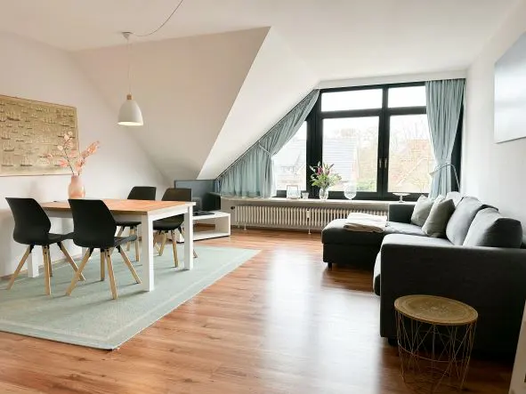 Bright living space with wood floors, a dining table with black chairs, and a gray sectional sofa near a large window with blue curtains.