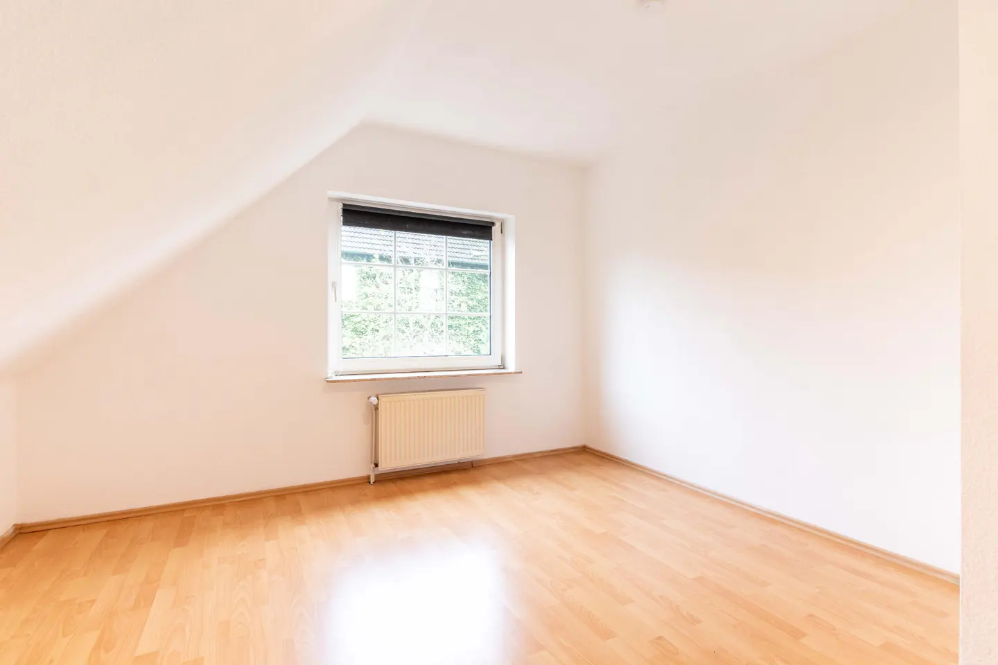 Bright, empty room with wood floor, white walls, and a window with blinds. A radiator sits beneath the window.