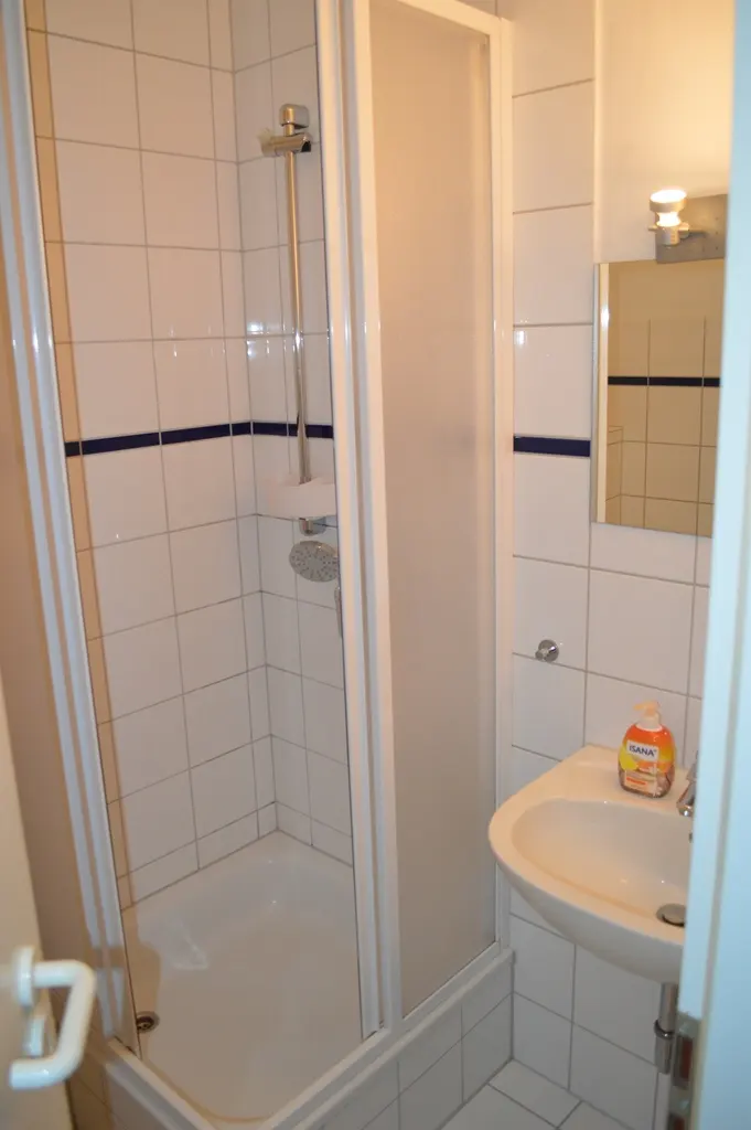 Bathroom with white tiled walls, a shower with a frosted glass door, and a white sink with soap.