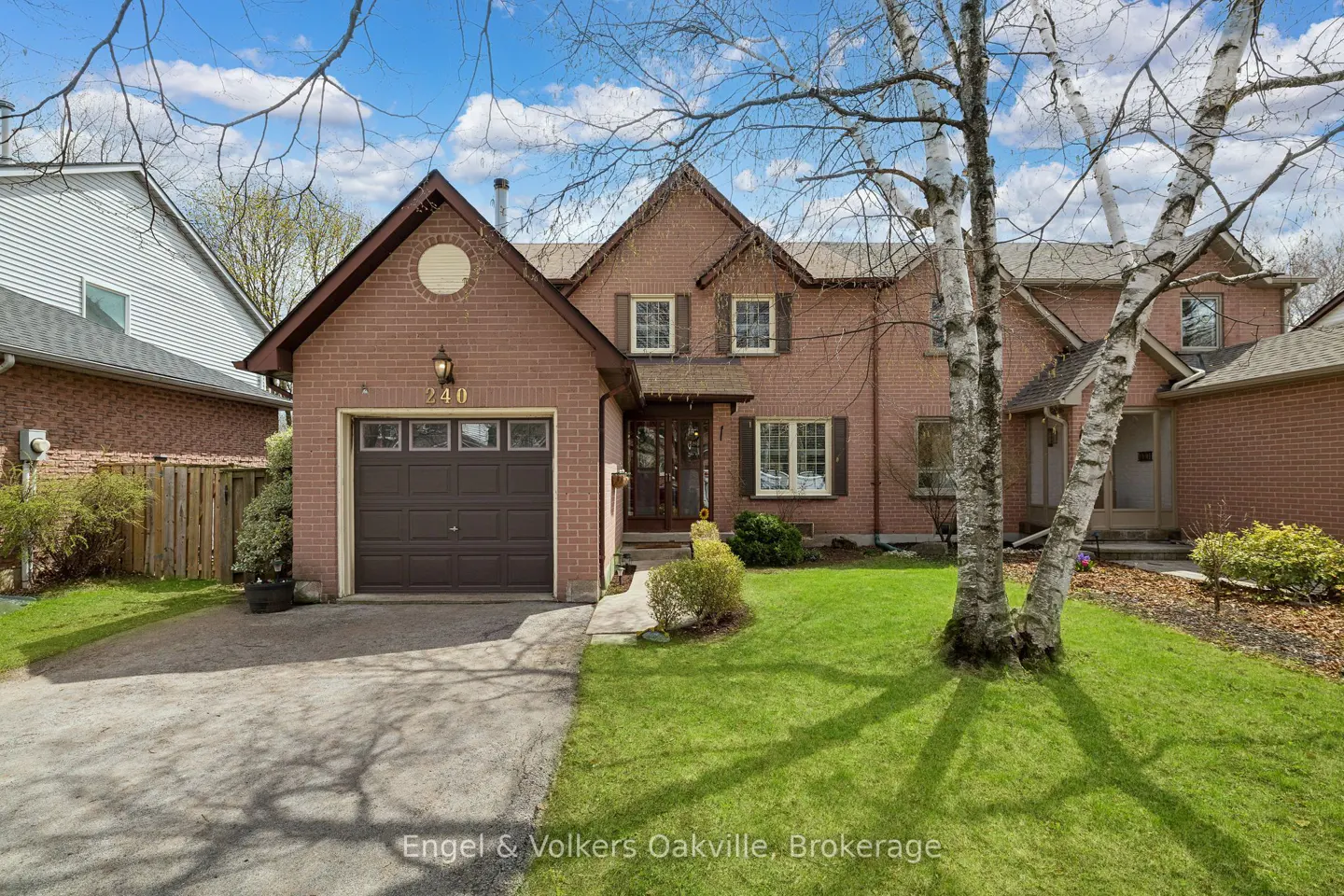 A two-story brick house with a brown garage door, green lawn, and birch trees in the front yard.