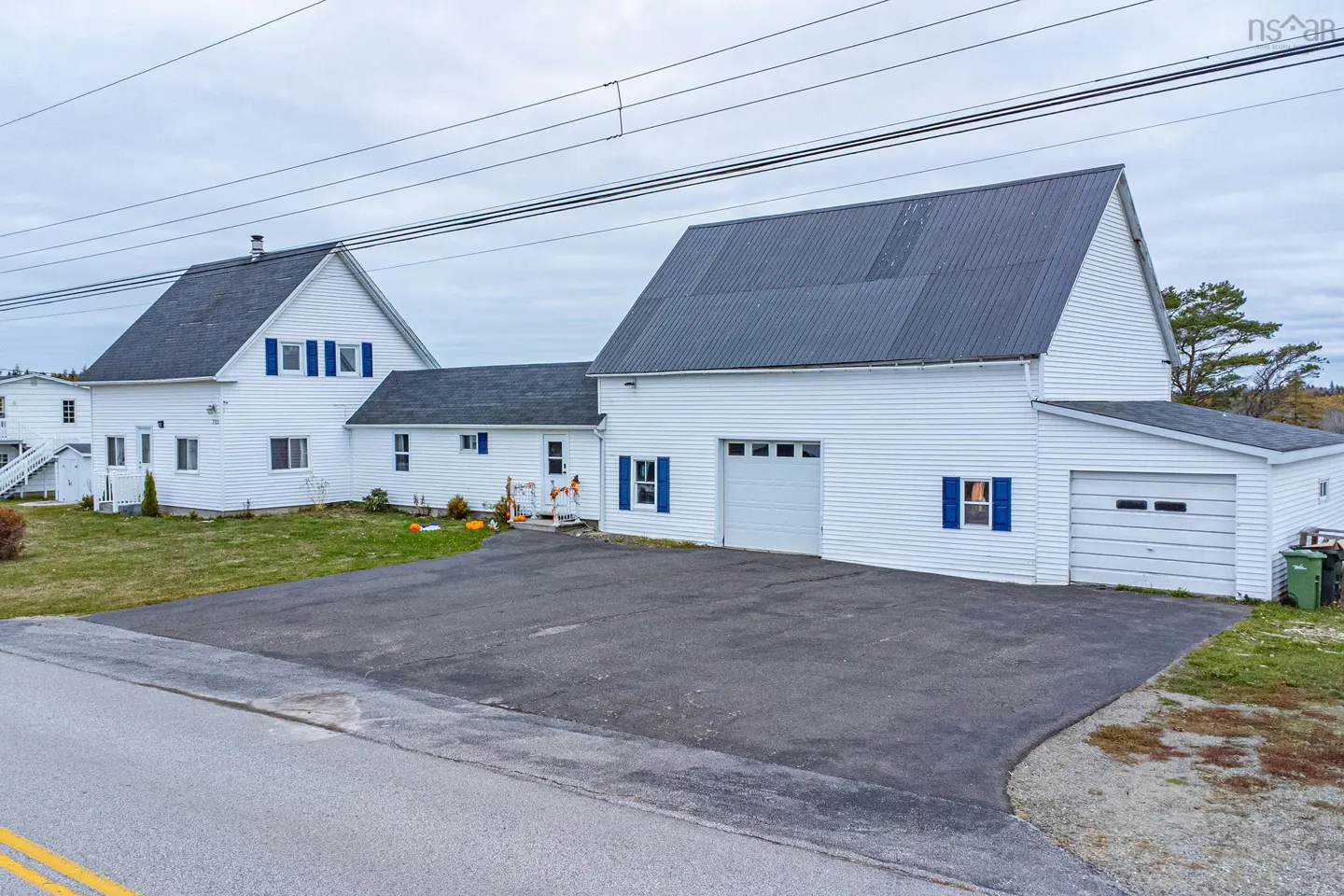 Exterior of a white clapboard house with blue shutters and a dark roof, featuring a large paved driveway.