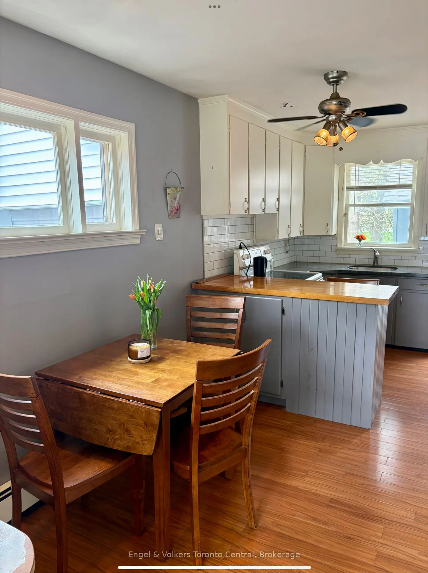 A kitchen with a wooden table, chairs, and a vase of tulips. White cabinets and a gray island are in the background.