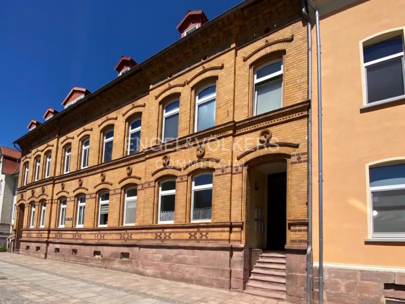 A three-story yellow brick building with arched windows, a stone base, and a small entrance staircase under a clear sky.