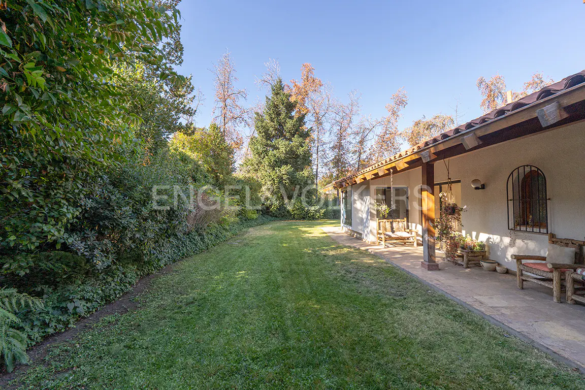 A house with a large green lawn and trees. The house has a porch with wooden furniture.