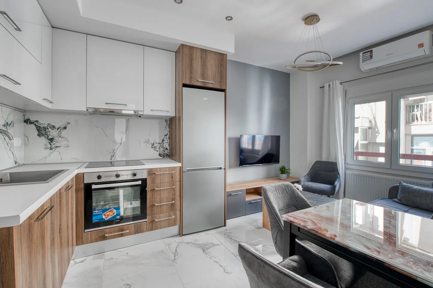 A modern apartment interior with white cabinets, stainless steel appliances, and a marble-topped dining table.