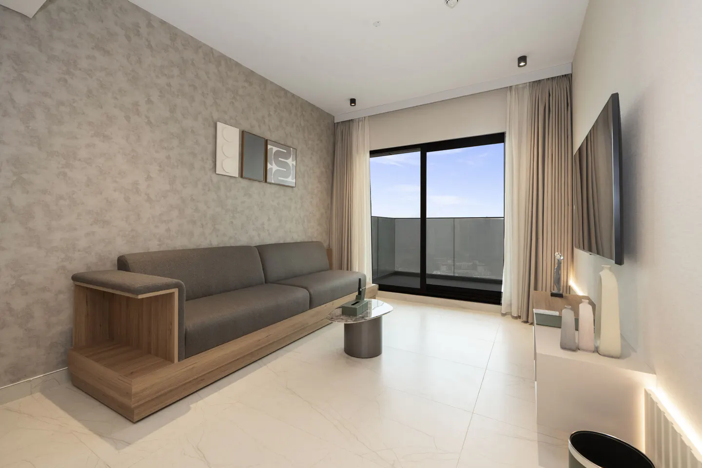 Living room with a gray sofa, wood trim, and a balcony with a view. A TV is mounted on the wall.