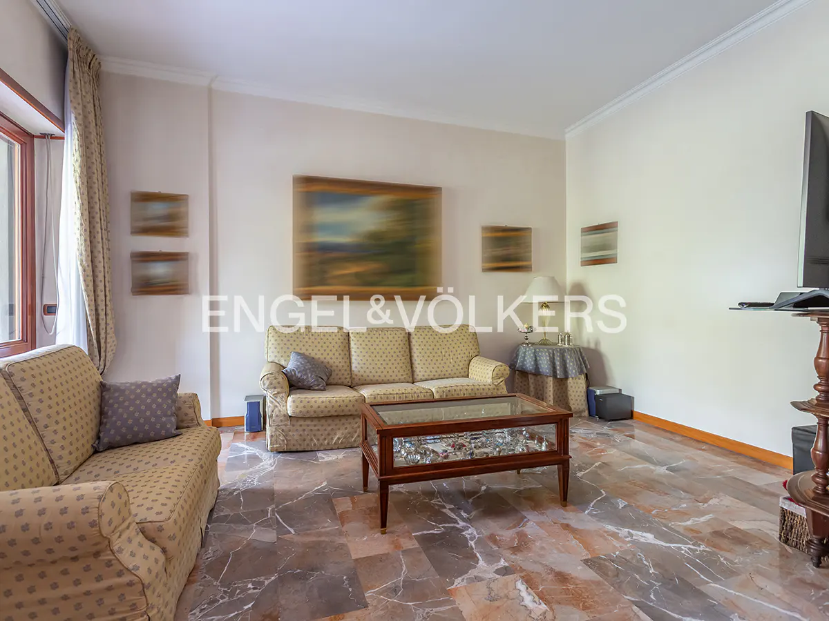 Living room with two patterned sofas, a glass-topped coffee table, and marble floors. Art hangs on the walls.