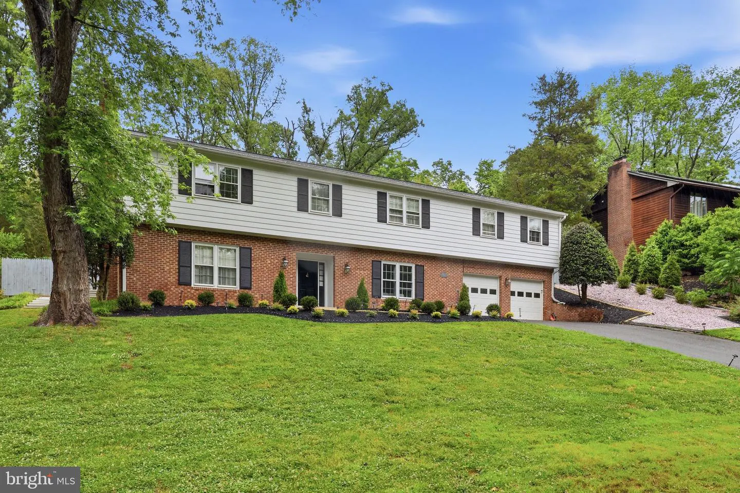 Two-story house with brick and white siding, black shutters, and a green lawn on a sunny day.