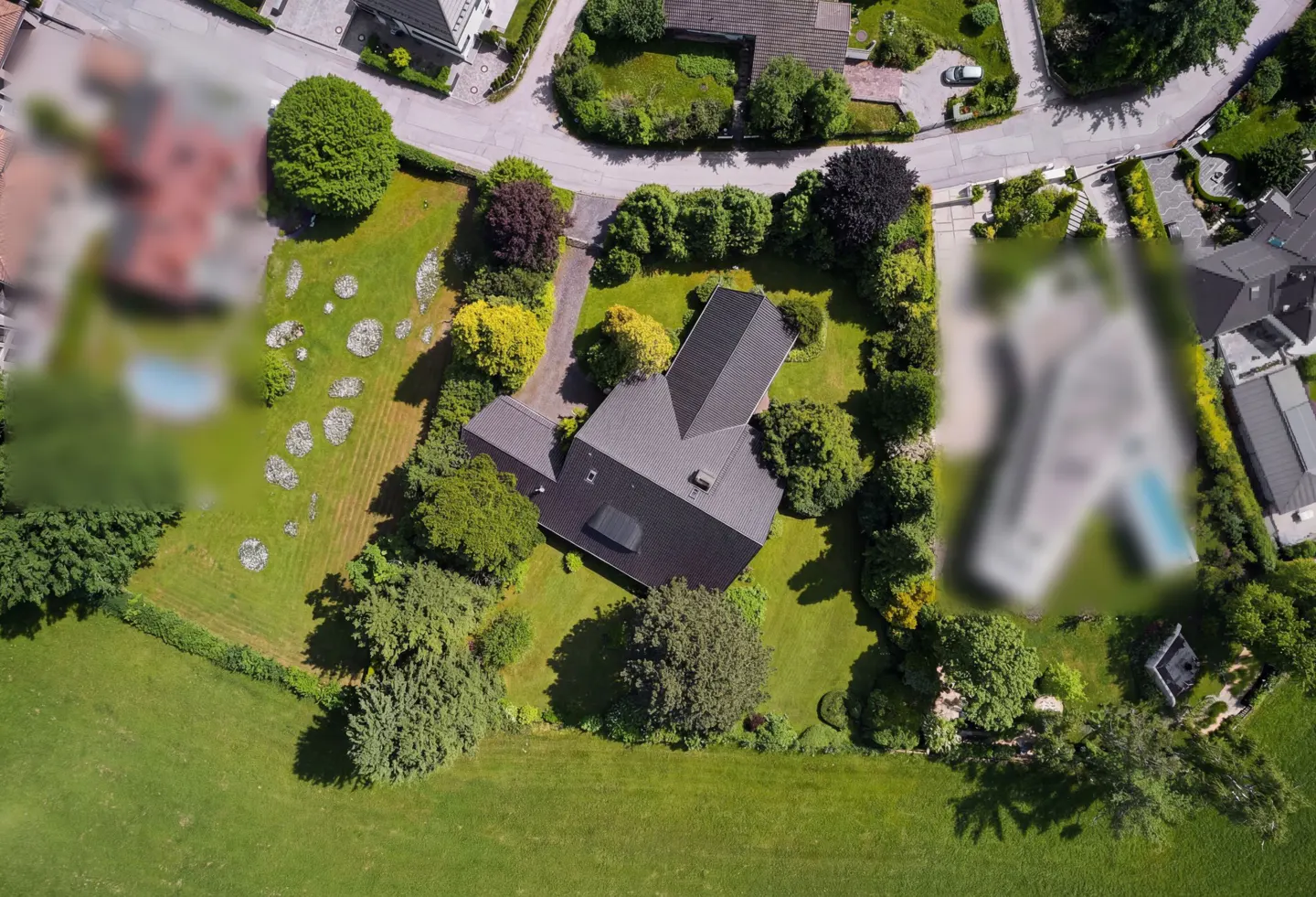 Aerial view of a modern house with a dark roof, surrounded by green trees and lawn.