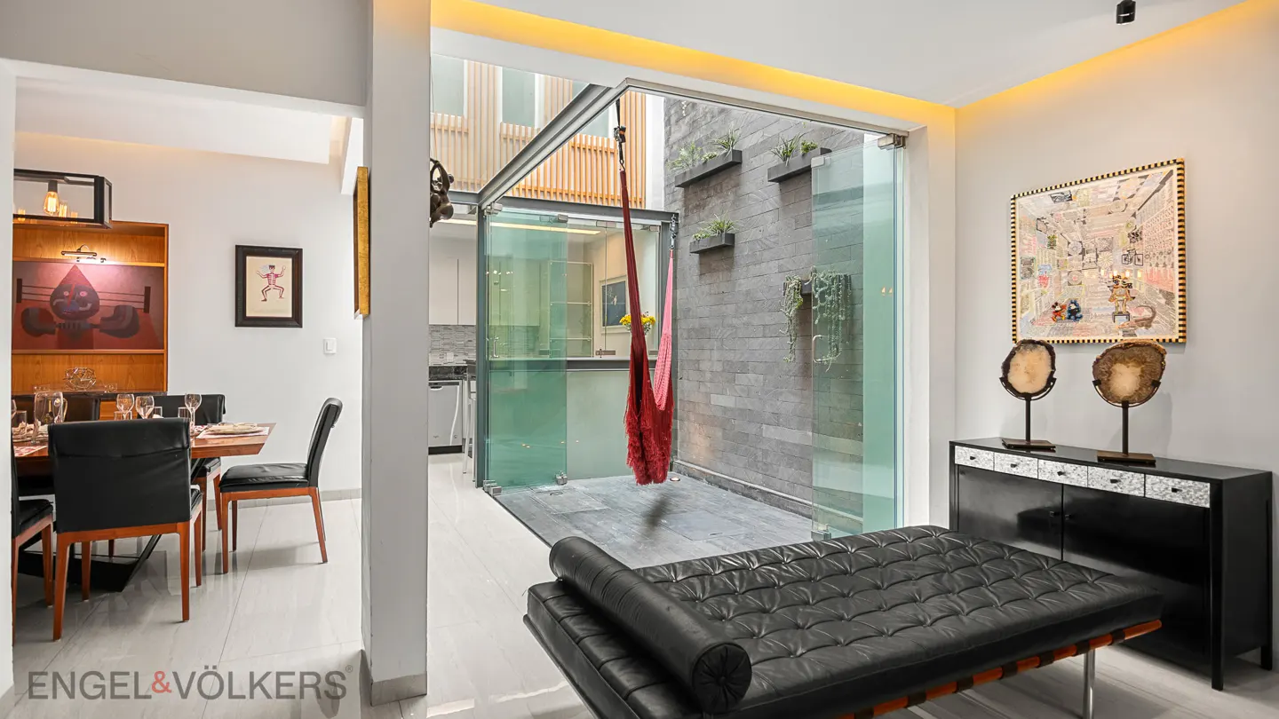 A modern home interior with a dining area, a black leather couch, and a courtyard with a red hammock.