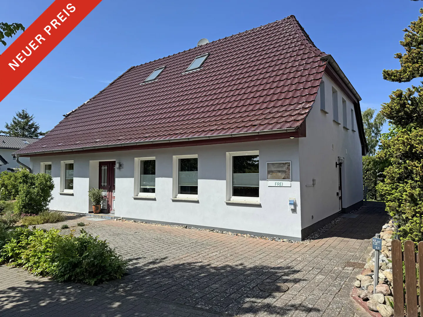 Two-story white house with a brown roof, a red "Neuer Preis" banner, and a paved driveway.