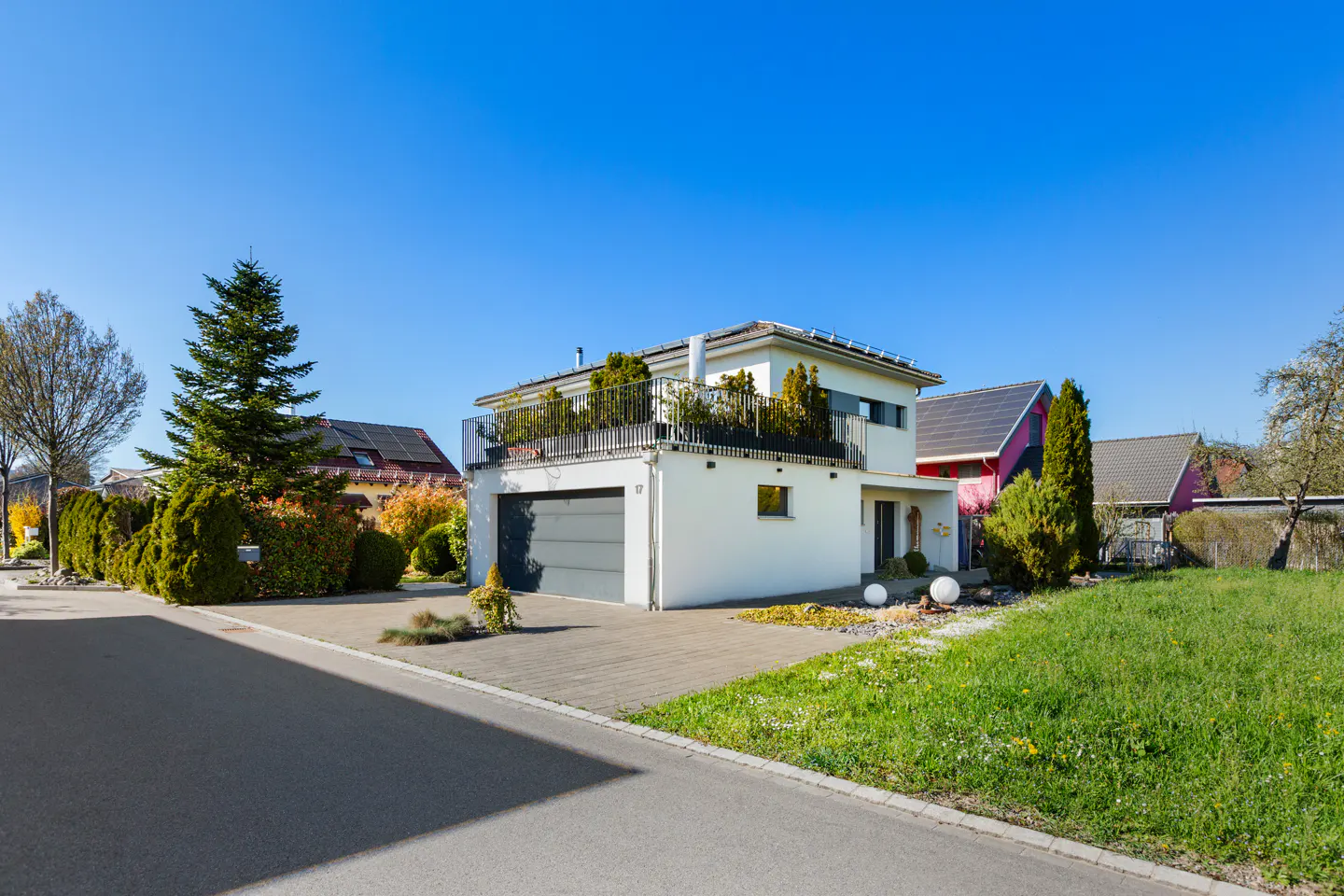 Two-story white house with a gray garage door and a rooftop terrace with plants, under a clear blue sky.