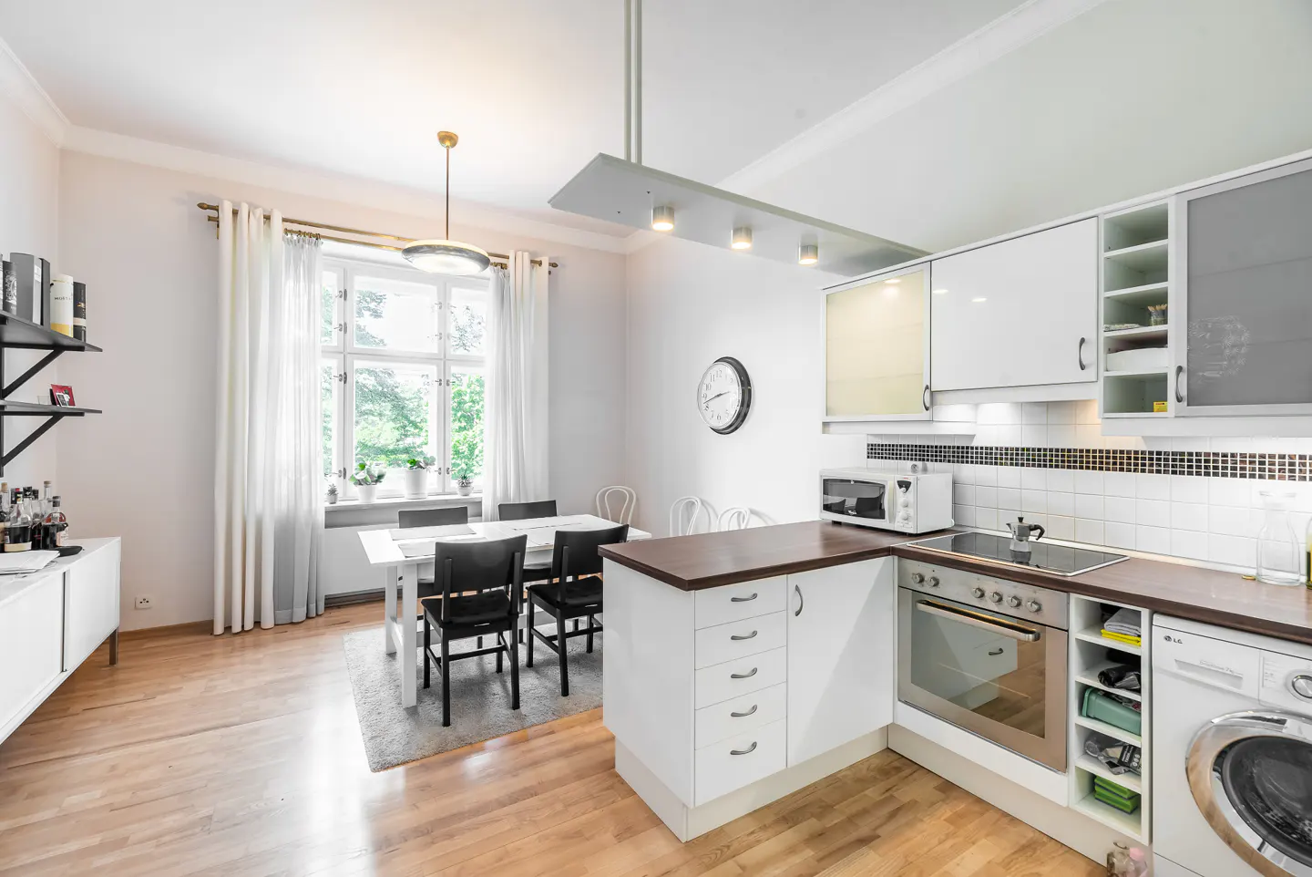 Bright, modern kitchen and dining area with white cabinets, wood floors, and a table set for six near a large window.