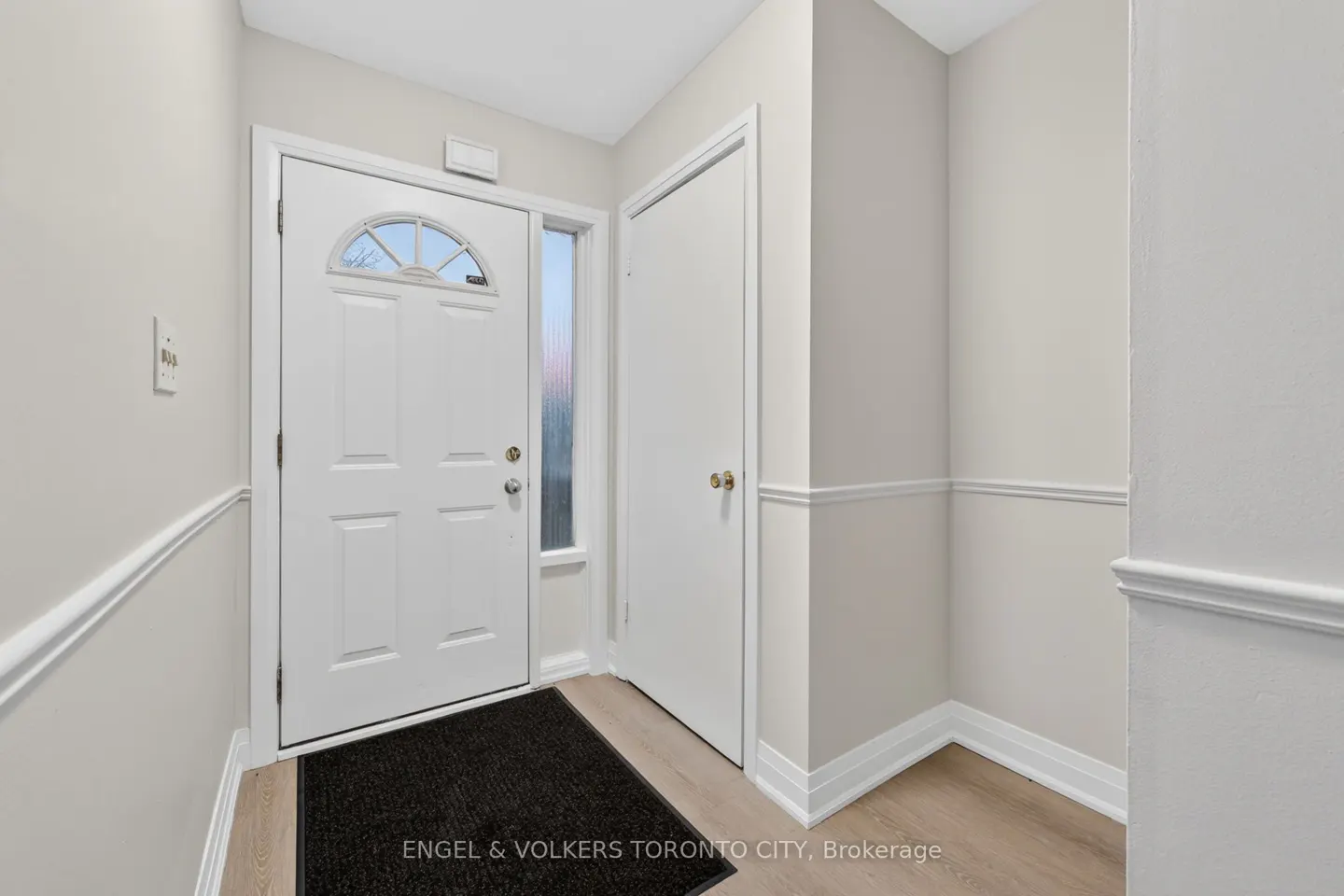 Entryway with a white front door, sidelight, and closet. A black mat sits on the light wood floor. Walls are light gray with white trim.