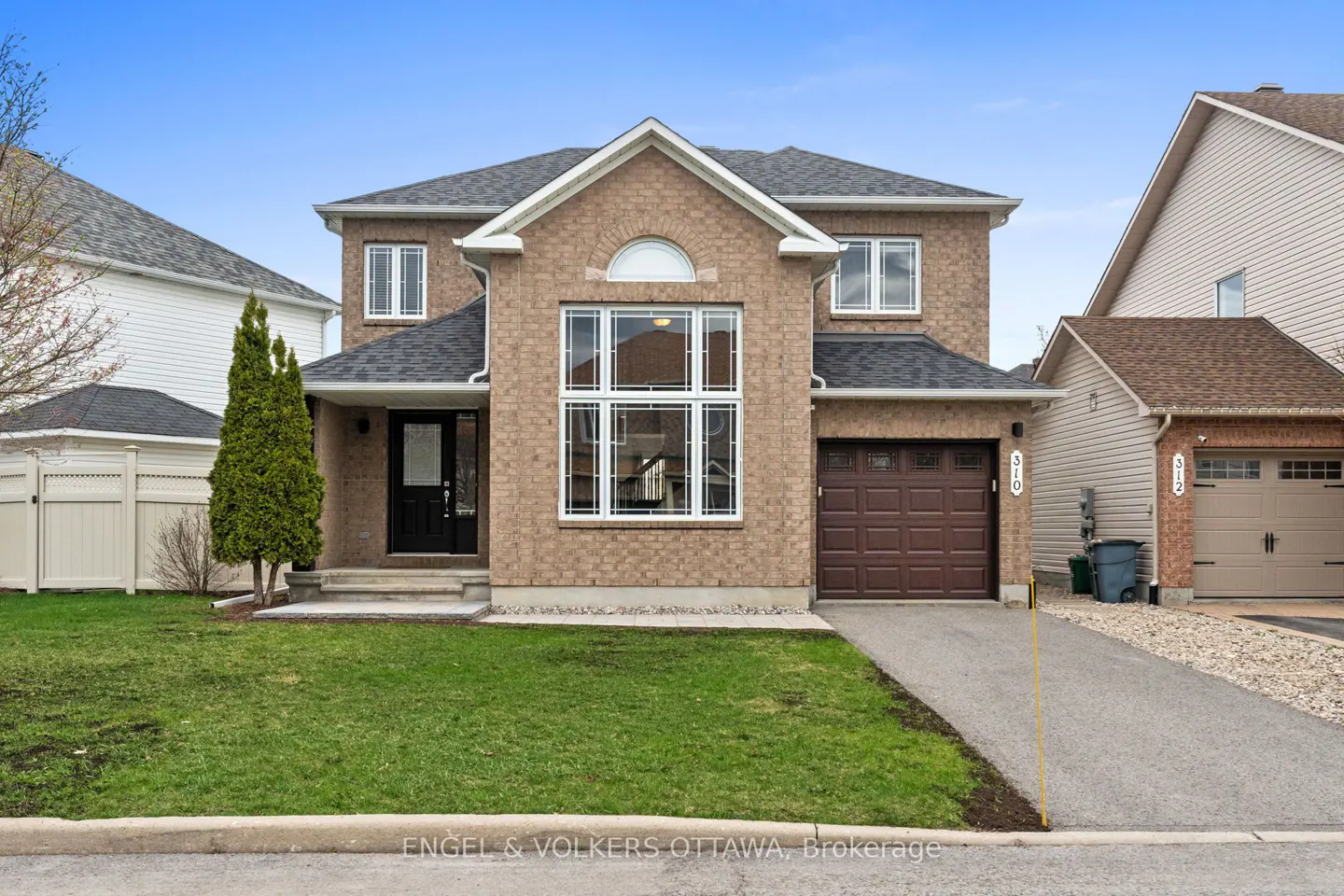 Two-story brick house with a black door, brown garage, and green lawn under a blue sky.