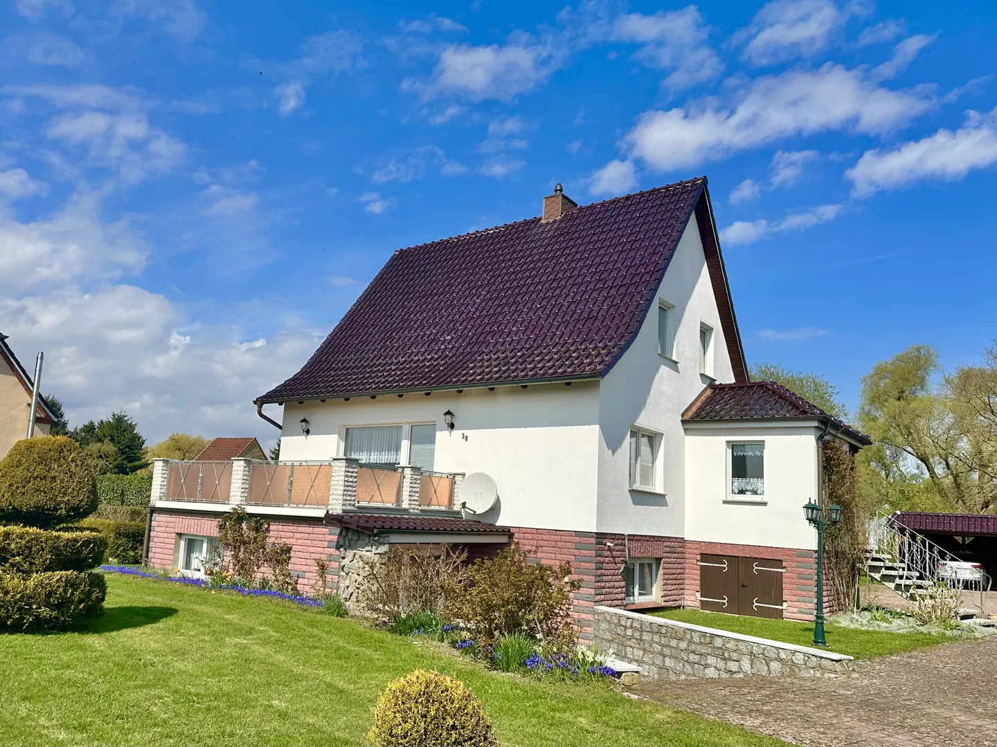 Two-story house with a dark roof, white walls, and a brick foundation on a green lawn under a blue sky.