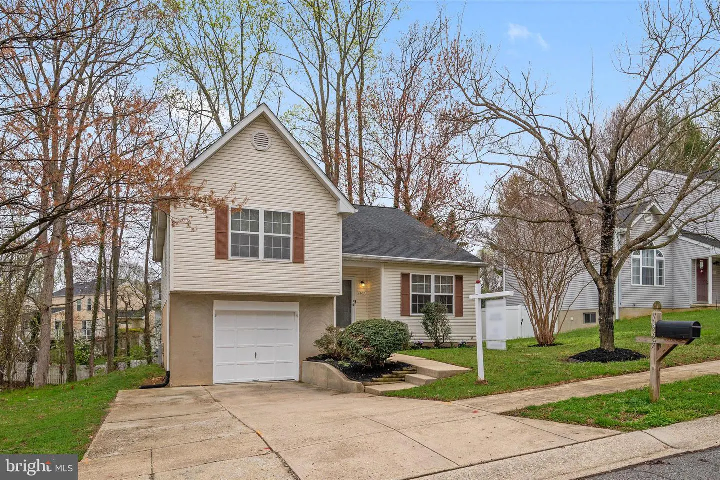Two-story beige house with brown shutters, a single-car garage, and a front yard with a real estate sign.