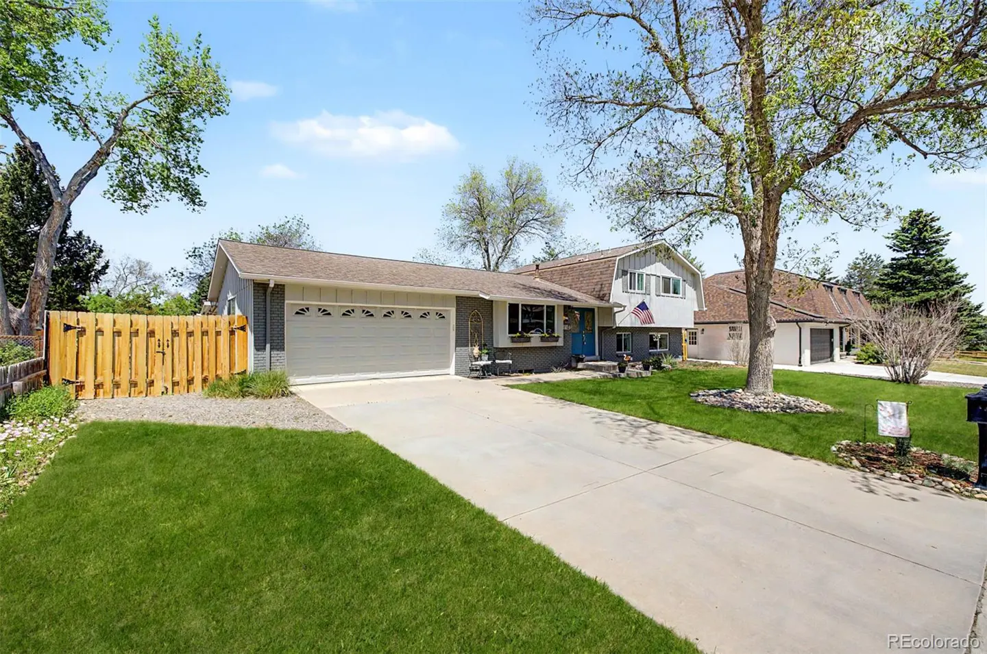 A single-family home with a gray brick facade, white garage door, blue front door, and green lawn.