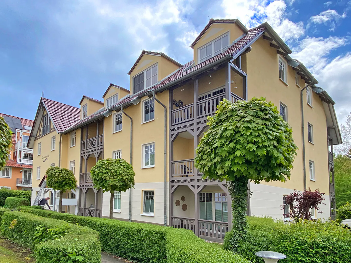Exterior view of a yellow apartment building with balconies and manicured green landscaping.